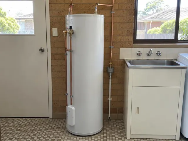 Tall white hot water cylinder beside a laundry sink and tiled wall in a home laundry in Kirrawee