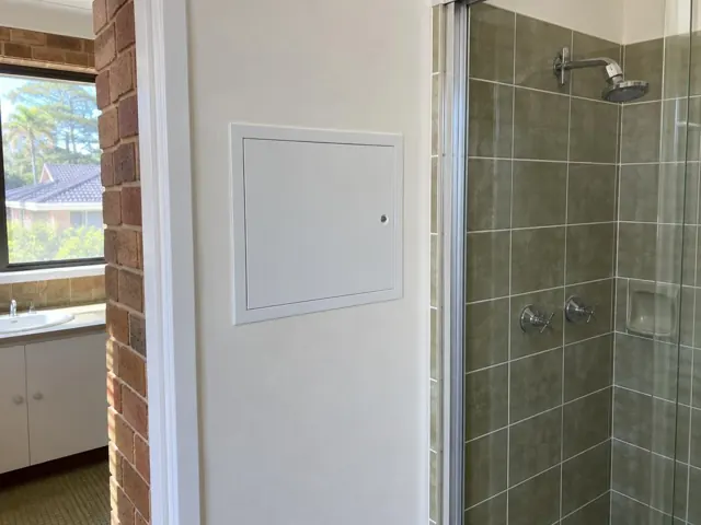 Bathroom wall with a small access panel beside a tiled shower and hallway doorway in Gymea Bay